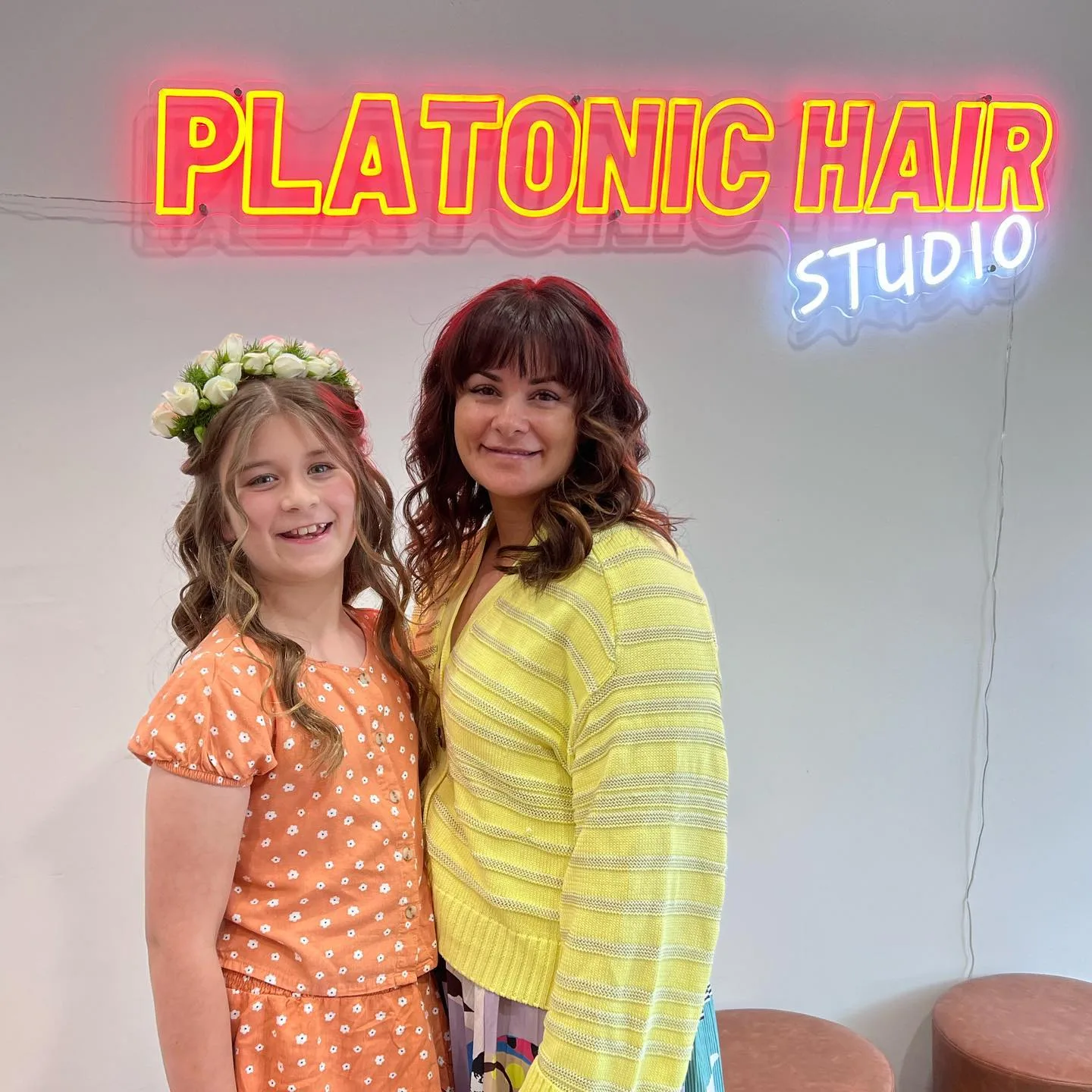 Auburn-curled woman and child in flower crown under Platonic Hair neon