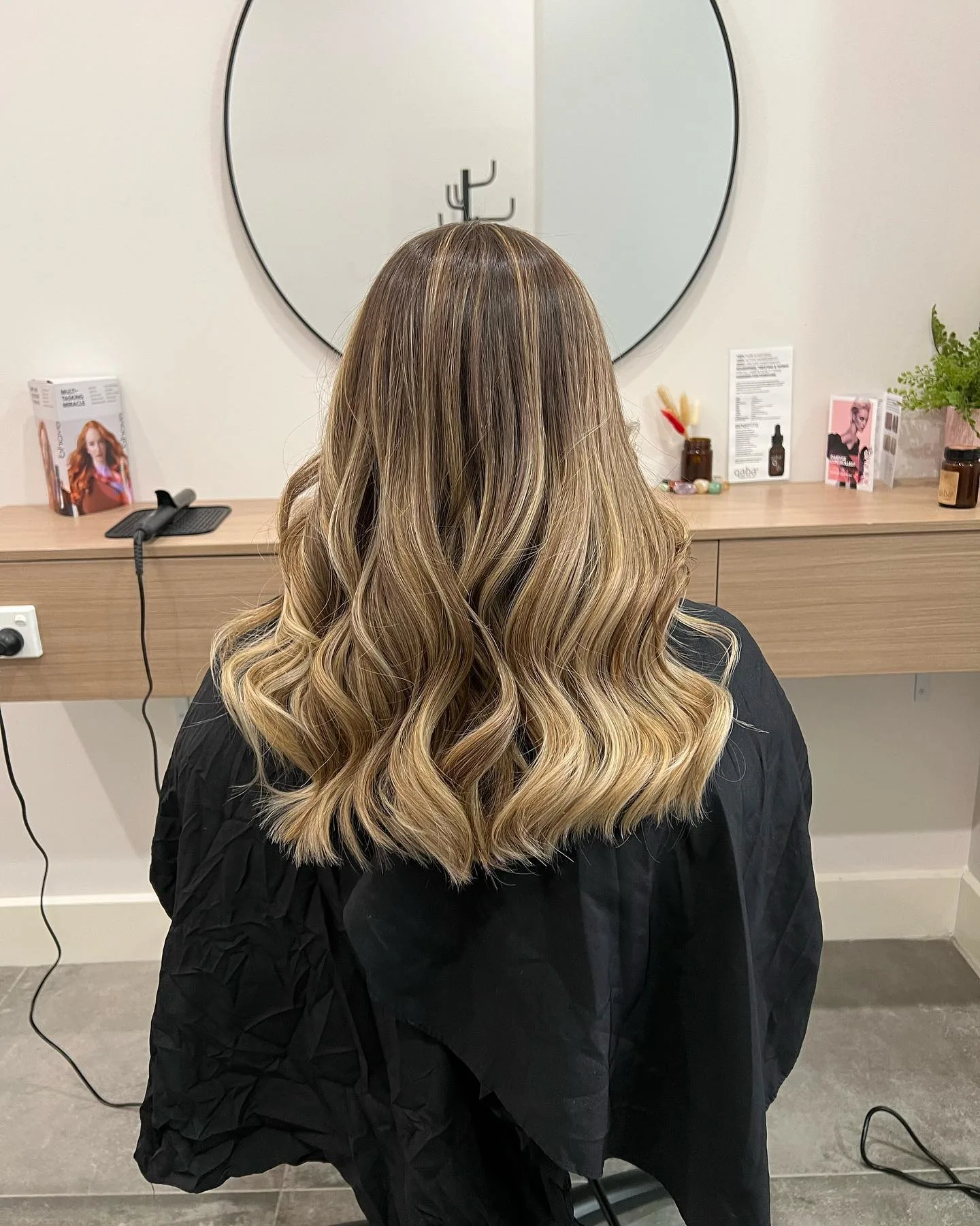 Long blonde balayage at a station with qaba shelf-cards behind