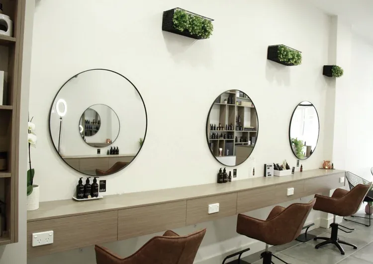 Platonic Hair Studio interior — three round mirrors over a pale-oak bench, tan leather chairs, black planter boxes of greenery