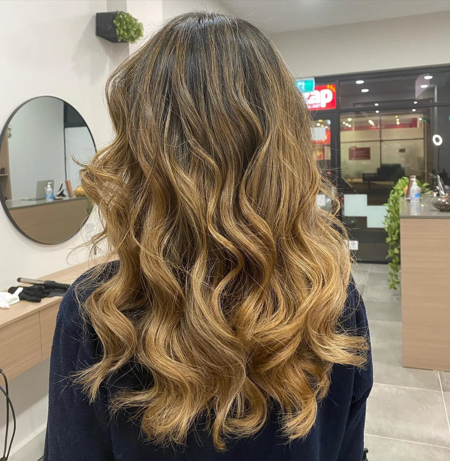 Long caramel balayage at night, lit shopfront behind